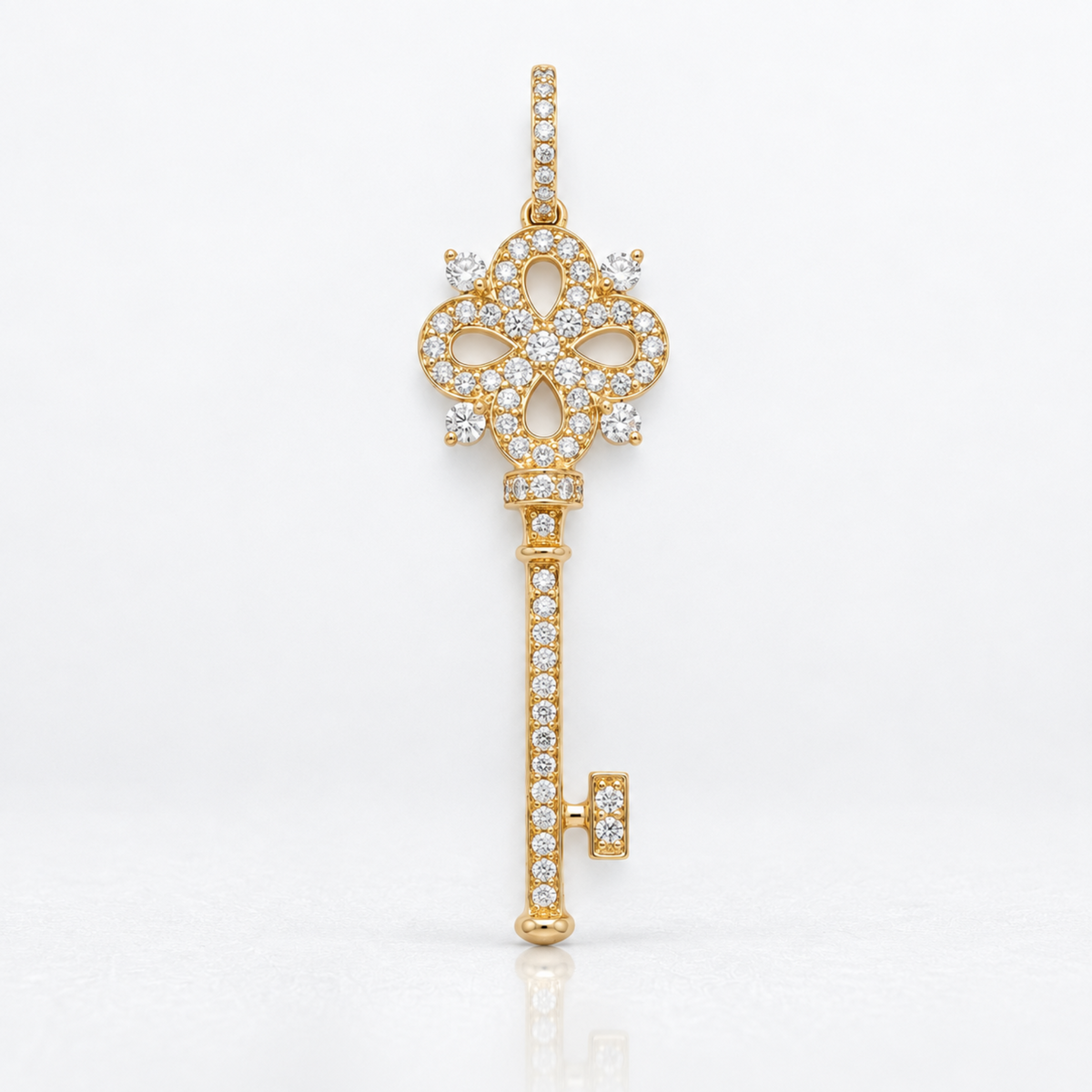 A gold key-shaped pendant or brooch adorned with clear pavé stones, photographed against a clean white background.