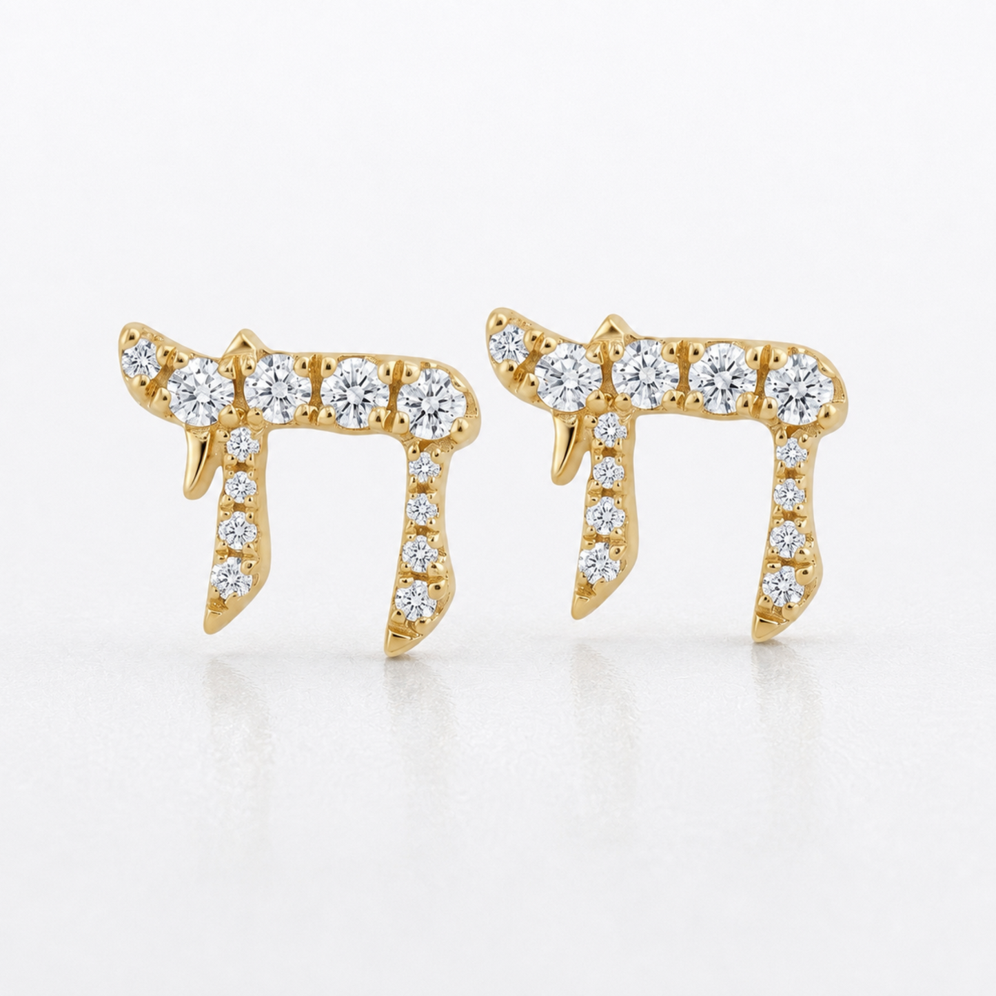 A pair of gold post earrings shaped like the Hebrew letter Shin, embellished with round and oval clear gemstones, set against a clean white background.