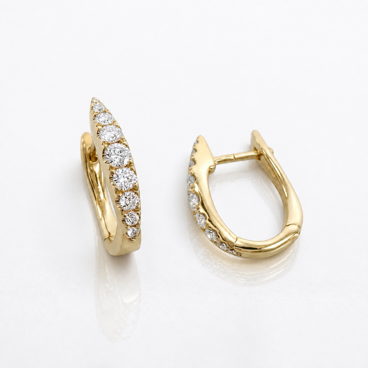 A pair of gold huggie hoop earrings with pavé-set round diamonds, shown from two angles on a clean white reflective surface.