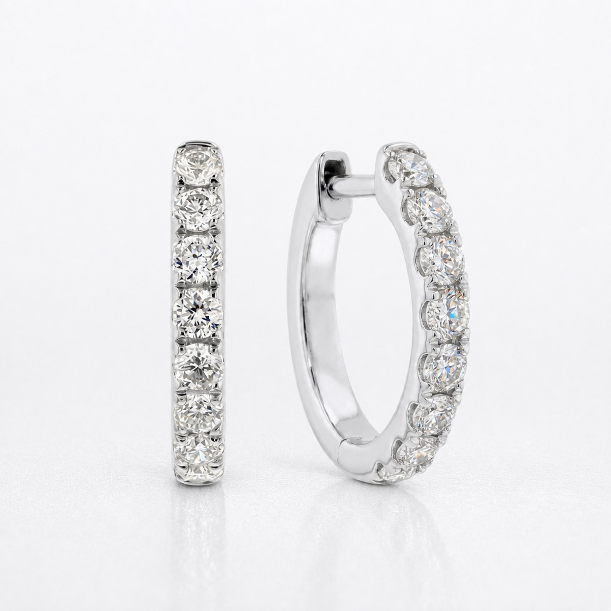 A pair of silver hoop earrings with a single row of round-cut clear diamonds, shown on a clean white background.