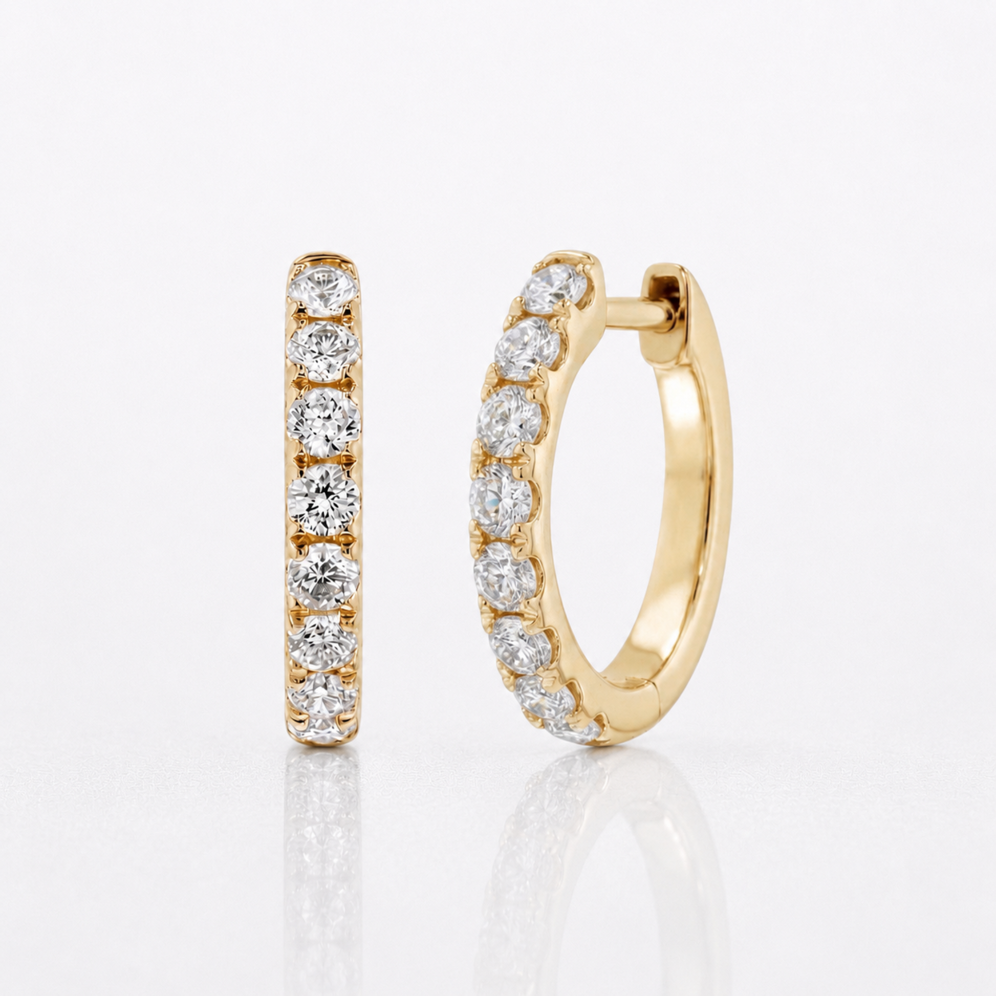 A pair of gold huggie hoop earrings, one shown front-facing and the other angled to show the side profile, both adorned with a row of round-cut clear diamonds, set against a clean white background with a soft reflection.