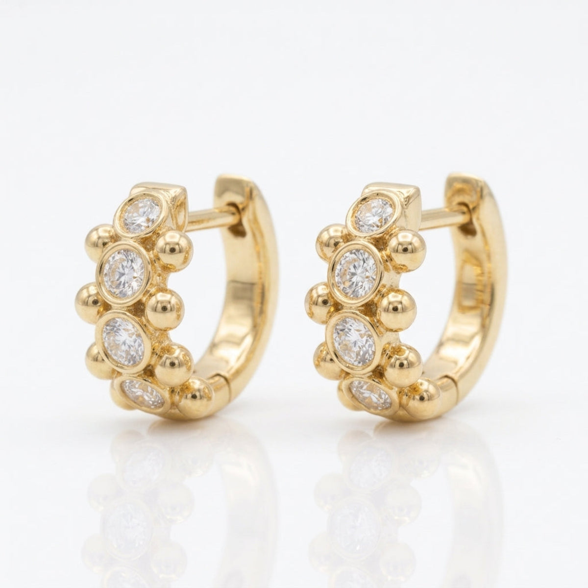 Angled view of 18K yellow gold Orbi Collection natural diamond bezel and gold bead huggie earrings