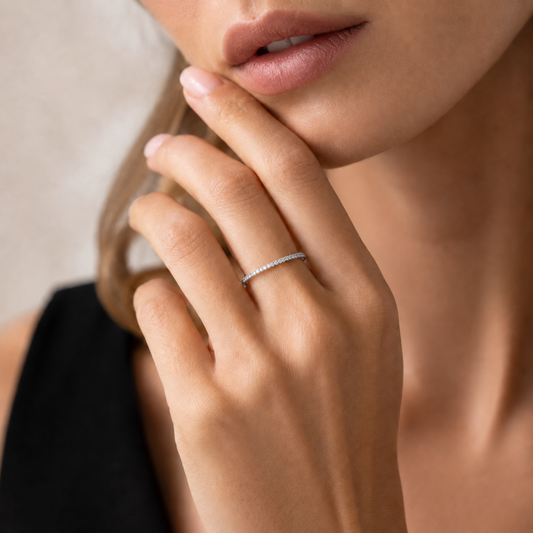 A close-up lifestyle shot of a woman wearing a delicate, thin silver band ring with a row of small clear diamonds on her ring finger.