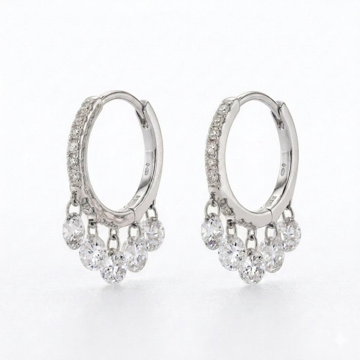 A pair of silver hoop earrings with small clear diamonds along the front and five clear dangling round diamonds stones on each earring, shown on a white background.