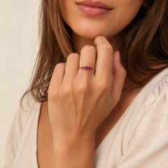 A close-up lifestyle shot of a woman wearing a delicate rose gold ring with a small, sparkling red rubies on her ring finger.