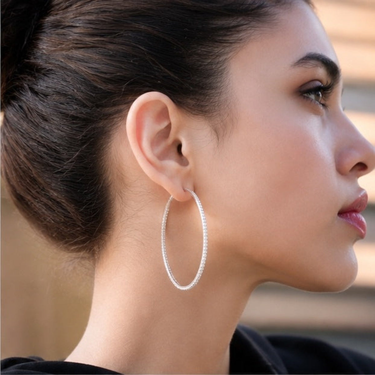 A close-up side profile of a woman wearing a large silver hoop earring with a textured, pavé-like surface.