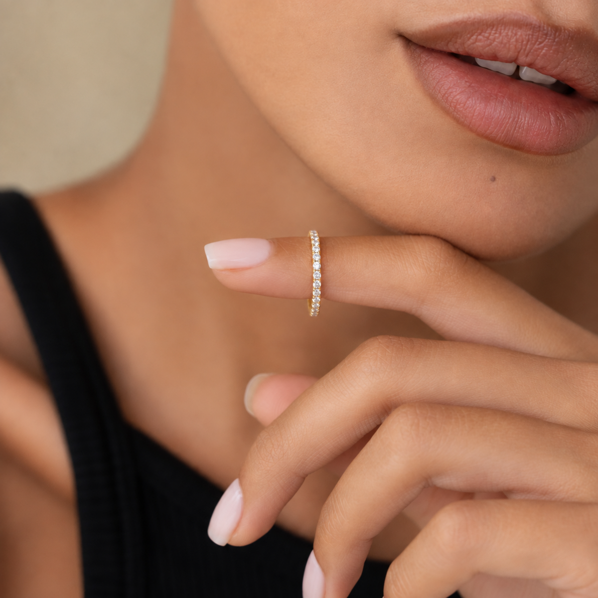 A close-up lifestyle shot of a model wearing a delicate gold eternity ring set with small diamonds on her index finger.