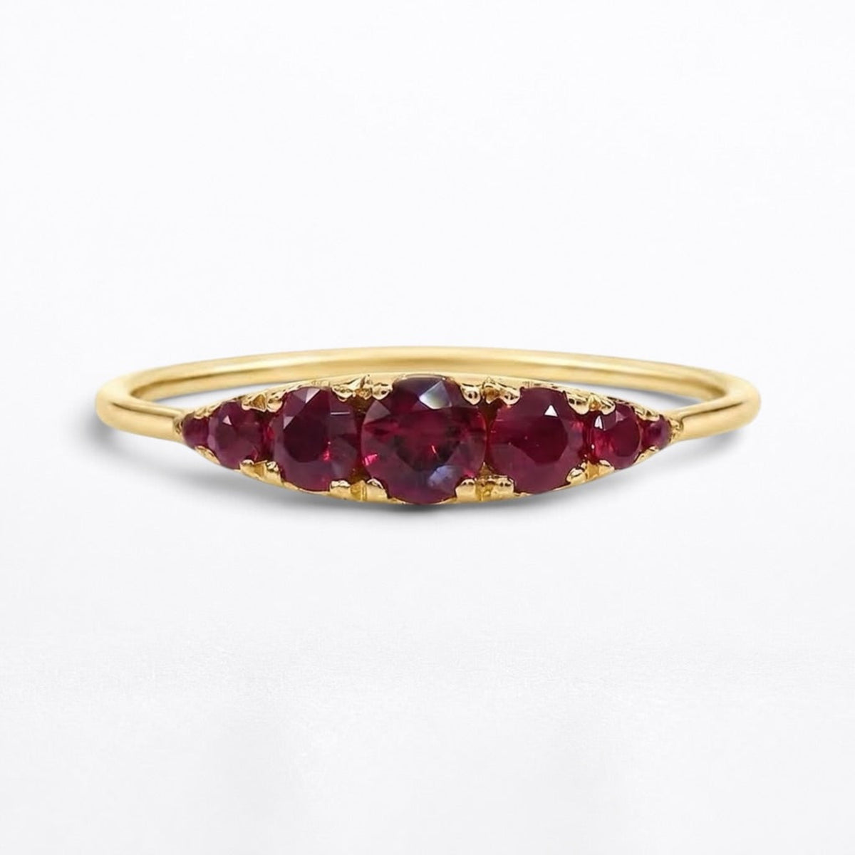 A yellow gold ring featuring five Graduated round-cut red rubies in a row, set against a clean white background.