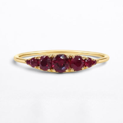 A yellow gold ring featuring five Graduated round-cut red rubies in a row, set against a clean white background.