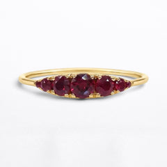 A yellow gold ring featuring five Graduated round-cut red rubies in a row, set against a clean white background.
