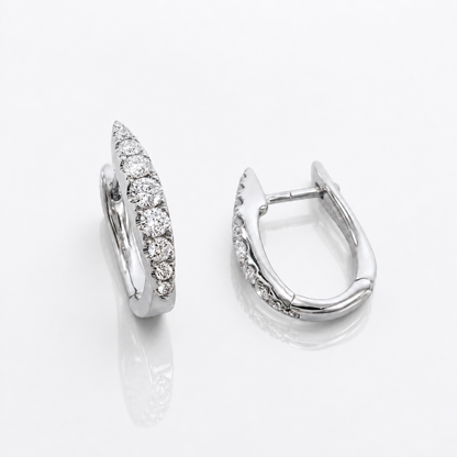 A pair of silver huggie hoop earrings with pavé-set round diamonds, shown from two angles on a reflective white surface.
