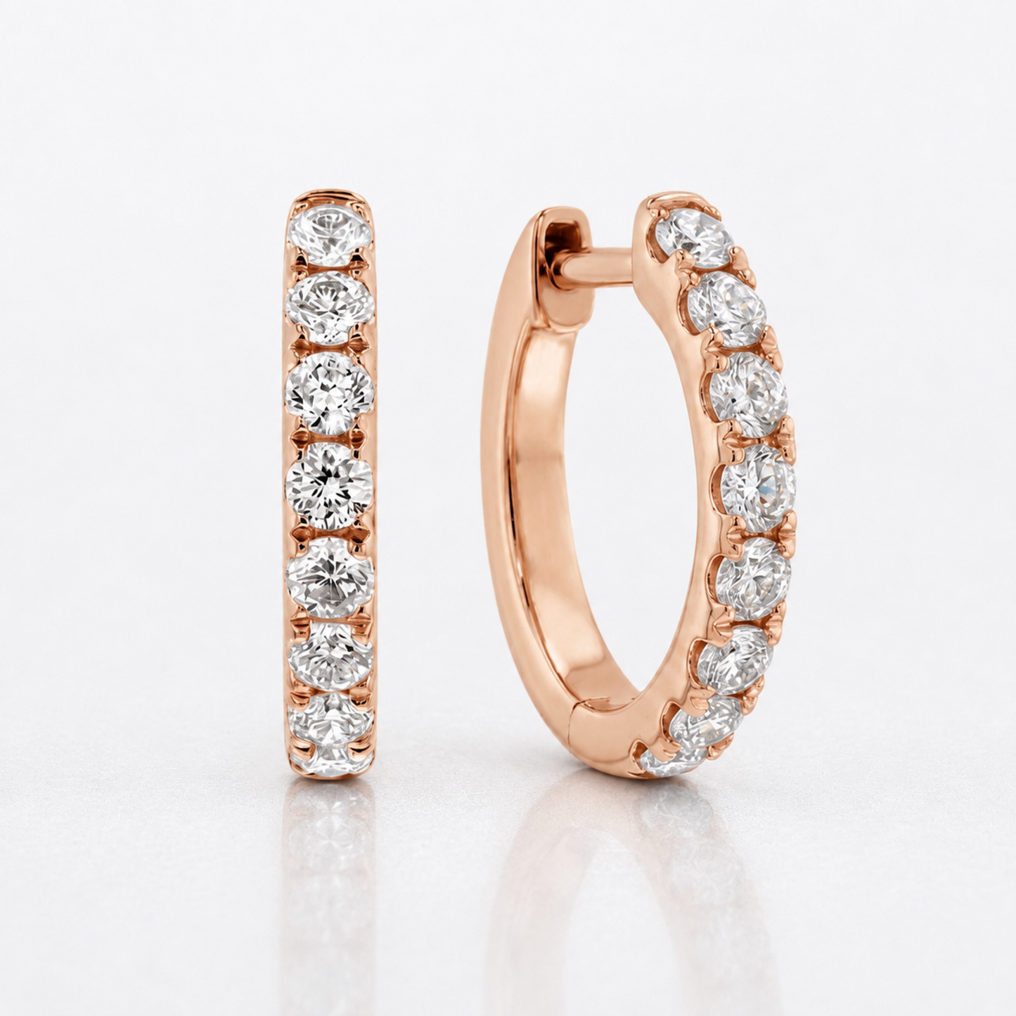 A pair of rose gold huggie hoop earrings, one shown flat and the other in profile, both adorned with a row of round-cut clear diamonds on a clean white background.