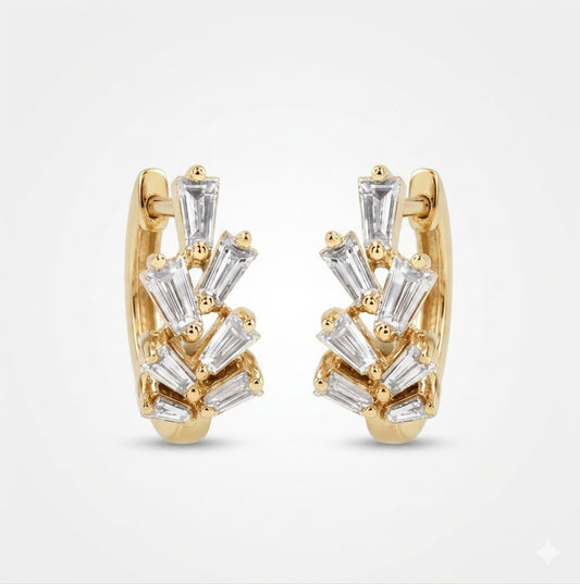 A pair of gold huggie hoop earrings decorated with clear baguette, shown against a light gray background.