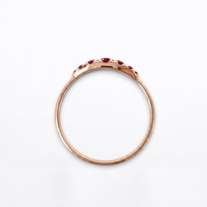 A rose gold ring with a delicate band and a row of small red rubies set along the top, photographed against a clean white background.
