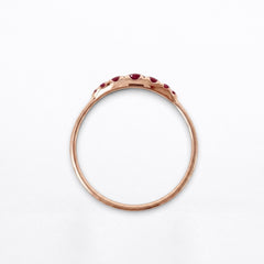 A rose gold ring with a delicate band and a row of small red rubies set along the top, photographed against a clean white background.