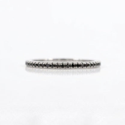 A thin silver-tone eternity ring set with small black diamonds, photographed on a clean white background with a soft reflection.
