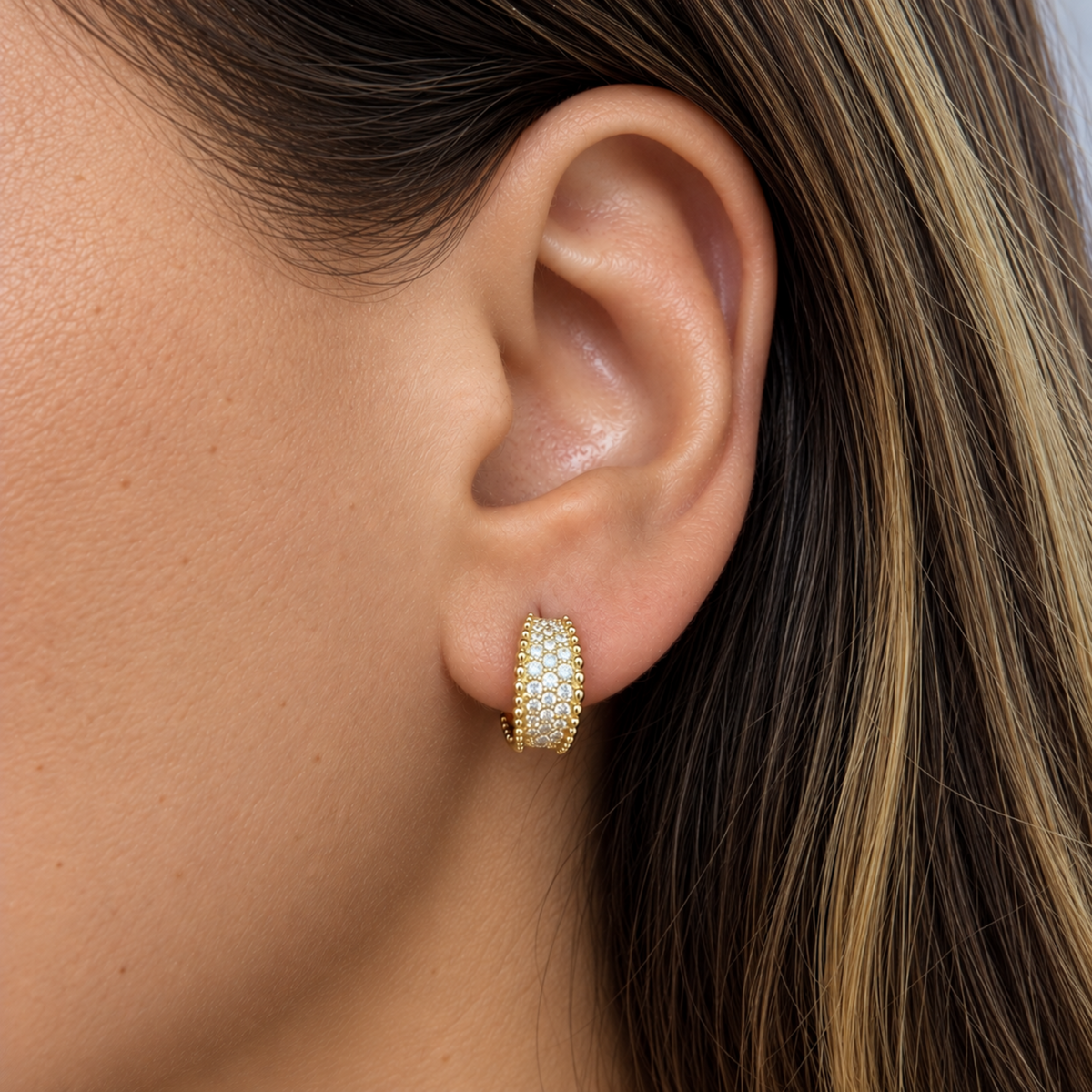 Close-up of a model wearing 12 mm yellow gold pavé natural diamond huggie hoop earrings with beaded gold edges.