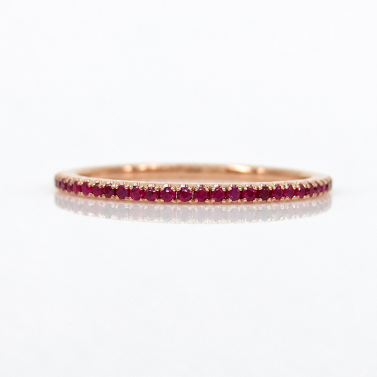 A rose gold eternity ring set with a row of round-cut red rubies, shown on a clean white reflective surface.