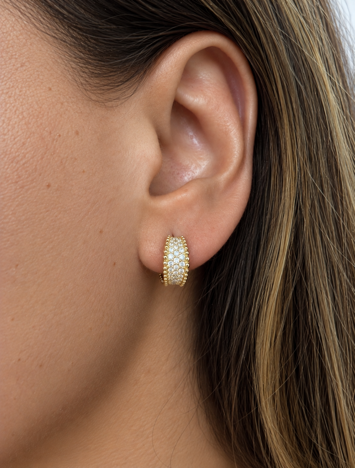 Side close-up of a model wearing a 12 mm yellow gold natural diamond pavé huggie hoop earring, featuring multiple rows of round diamonds and polished gold beaded edges.