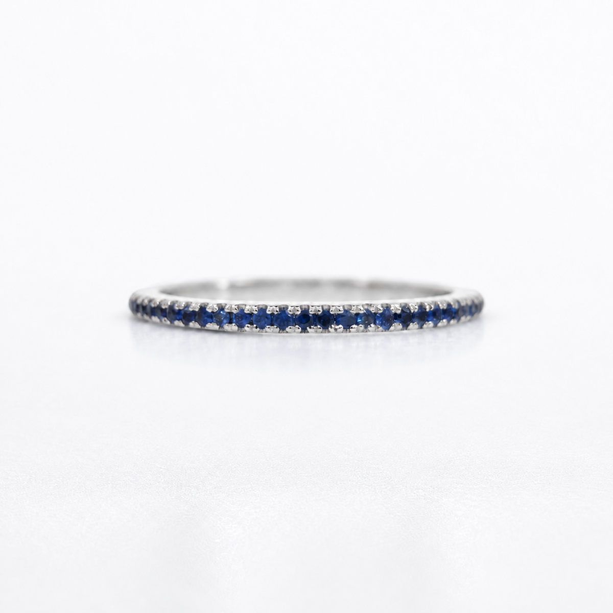 A thin silver-toned eternity ring set with small round blue sapphires and clear stones, photographed on a clean white background.