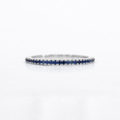 A thin silver-toned eternity ring set with small round blue sapphires and clear stones, photographed on a clean white background.