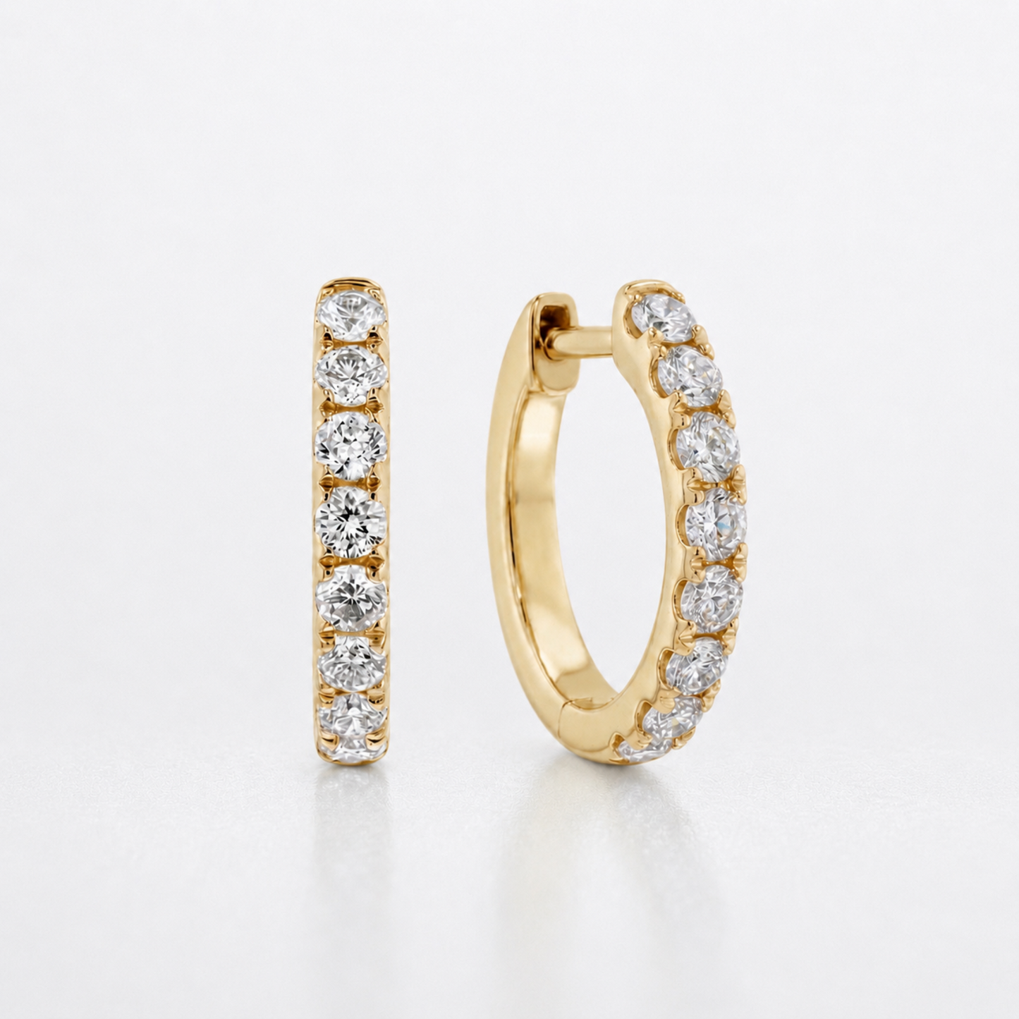 A pair of gold huggie hoop earrings with a channel-set row of round diamonds, shown on a clean white background.