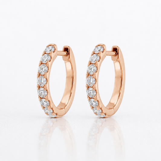 A pair of rose gold hoop earrings with a row of round-cut clear diamonds, displayed on a clean white reflective surface.