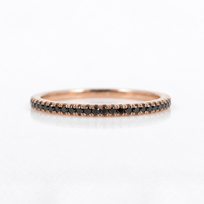 A thin rose gold eternity ring set with small round black diamonds, shown on a clean white background with a soft reflection.