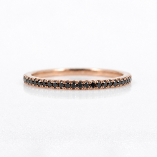 A thin rose gold eternity ring set with small round black diamonds, shown on a clean white background with a soft reflection.