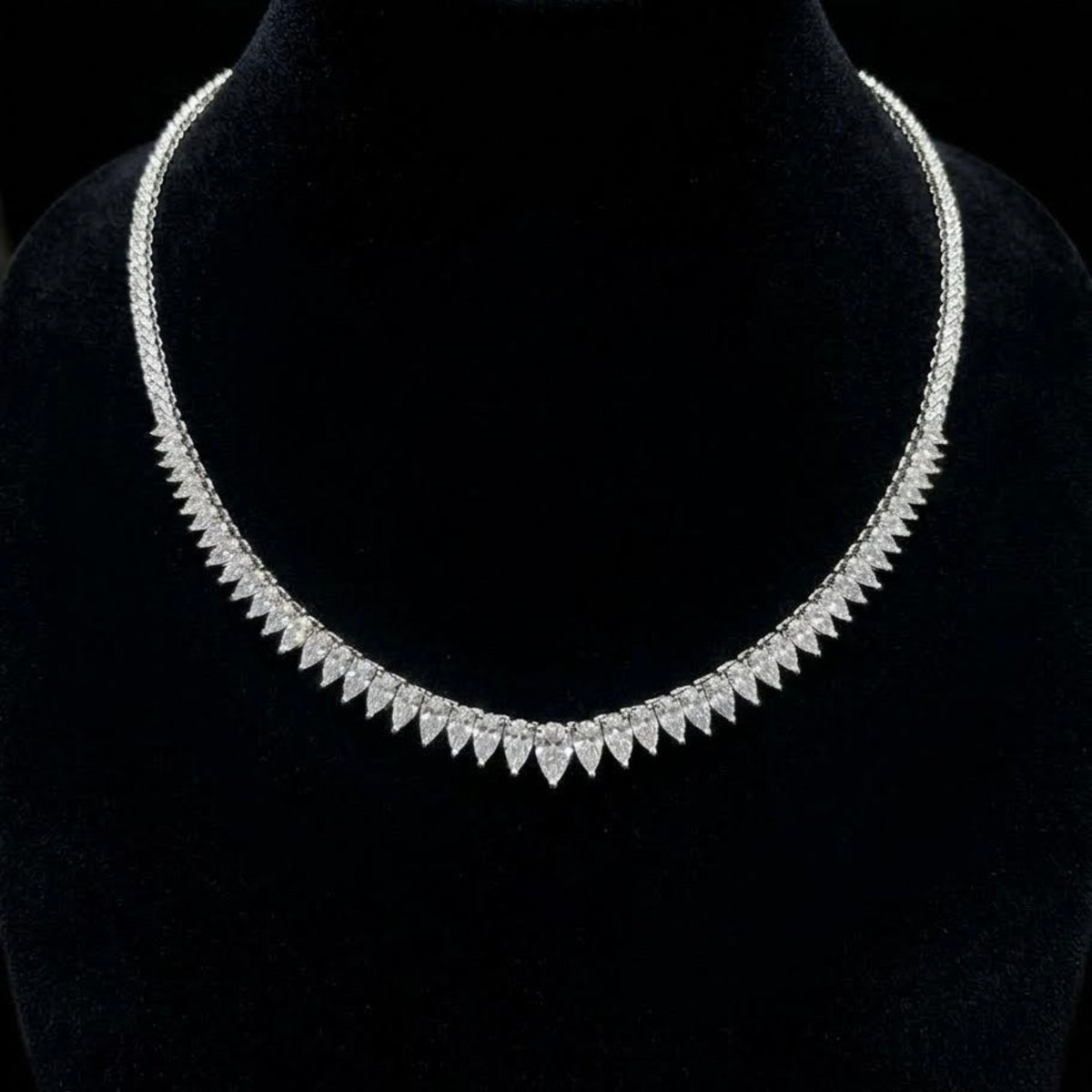 Pear-shaped and round natural diamond tennis necklace in 18K white gold displayed on a black velvet bust