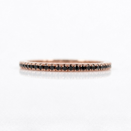 A delicate rose gold eternity ring featuring a row of small black diamonds, photographed on a clean white reflective surface.
