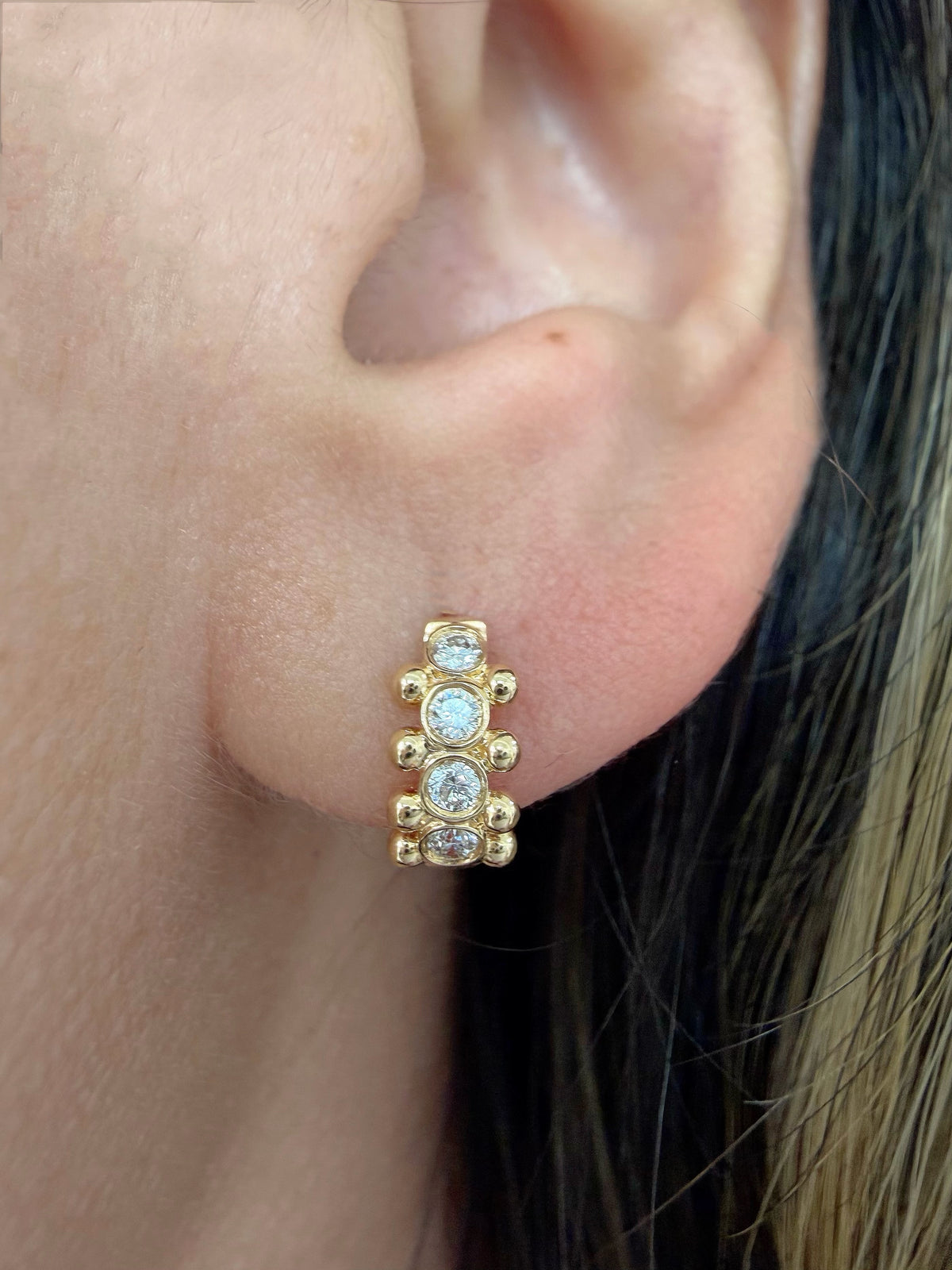 Close-up of model wearing 10mm 18K yellow gold Orbi natural diamond bezel and gold bead huggie earring