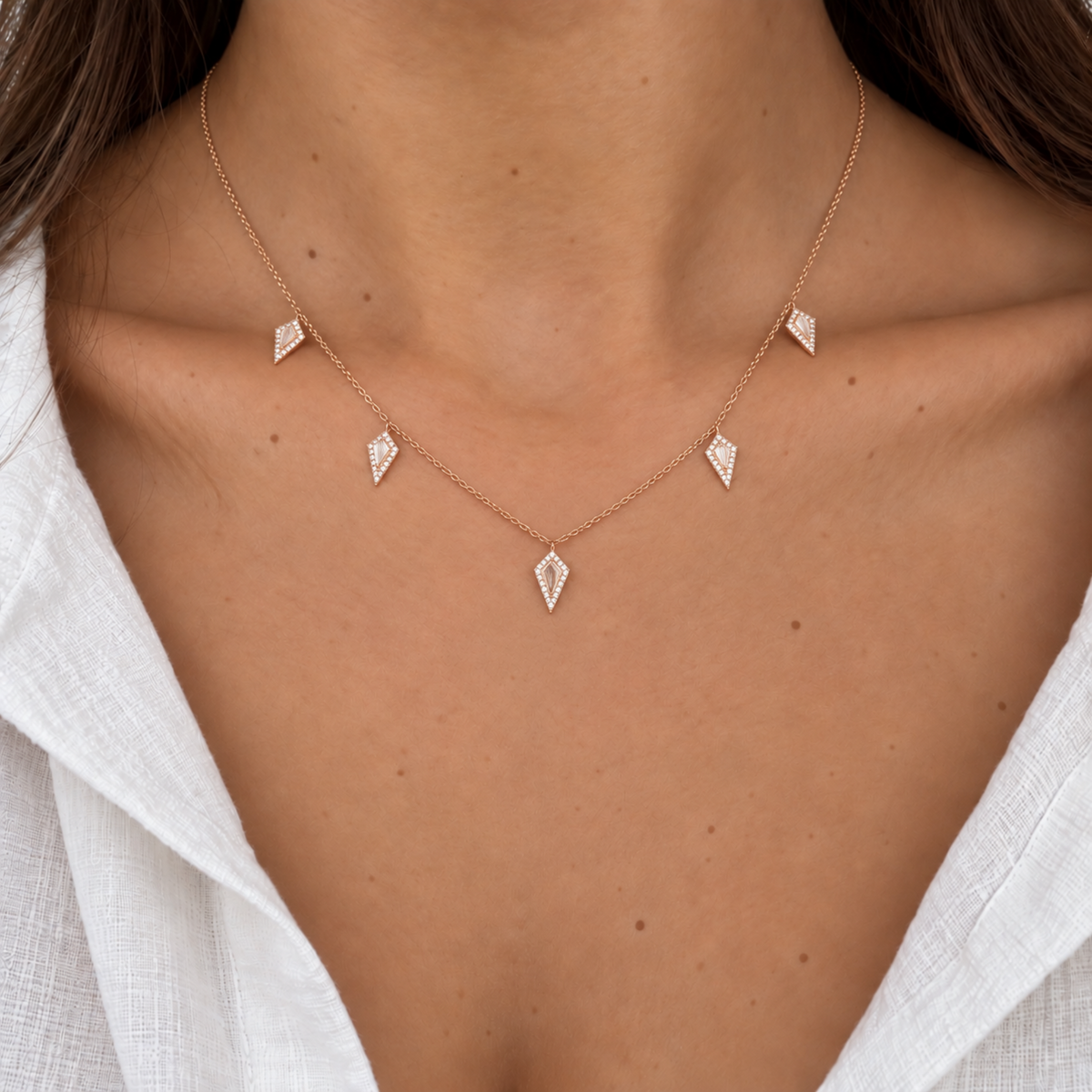 Close-up of a model wearing the 14K rose gold five kite charm necklace with natural diamonds over a white blouse.