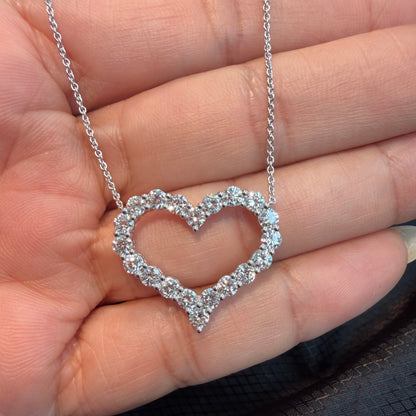 A silver heart-shaped pendant necklace paved with small clear diamonds, held in a person's hand.