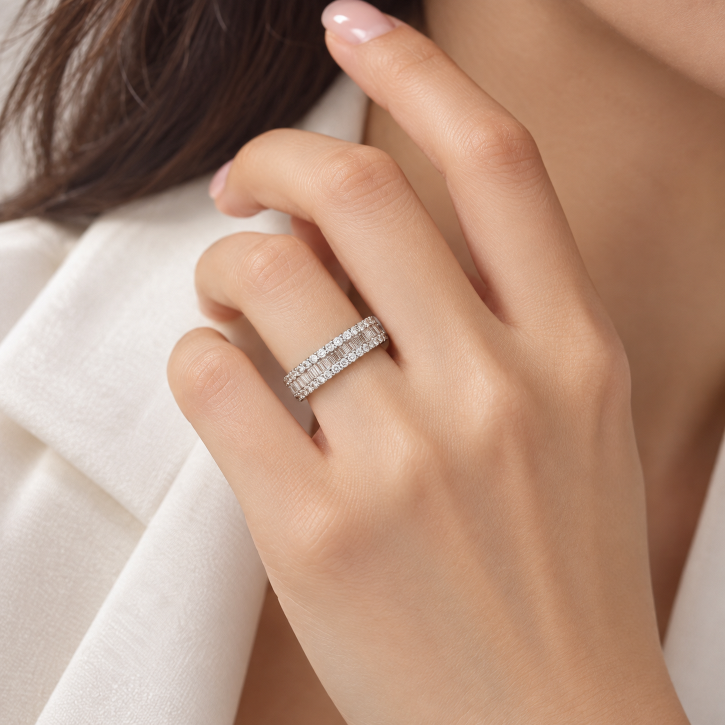 A close-up of a woman's hand wearing a silver band ring set with small clear diamonds, styled with a white blazer.