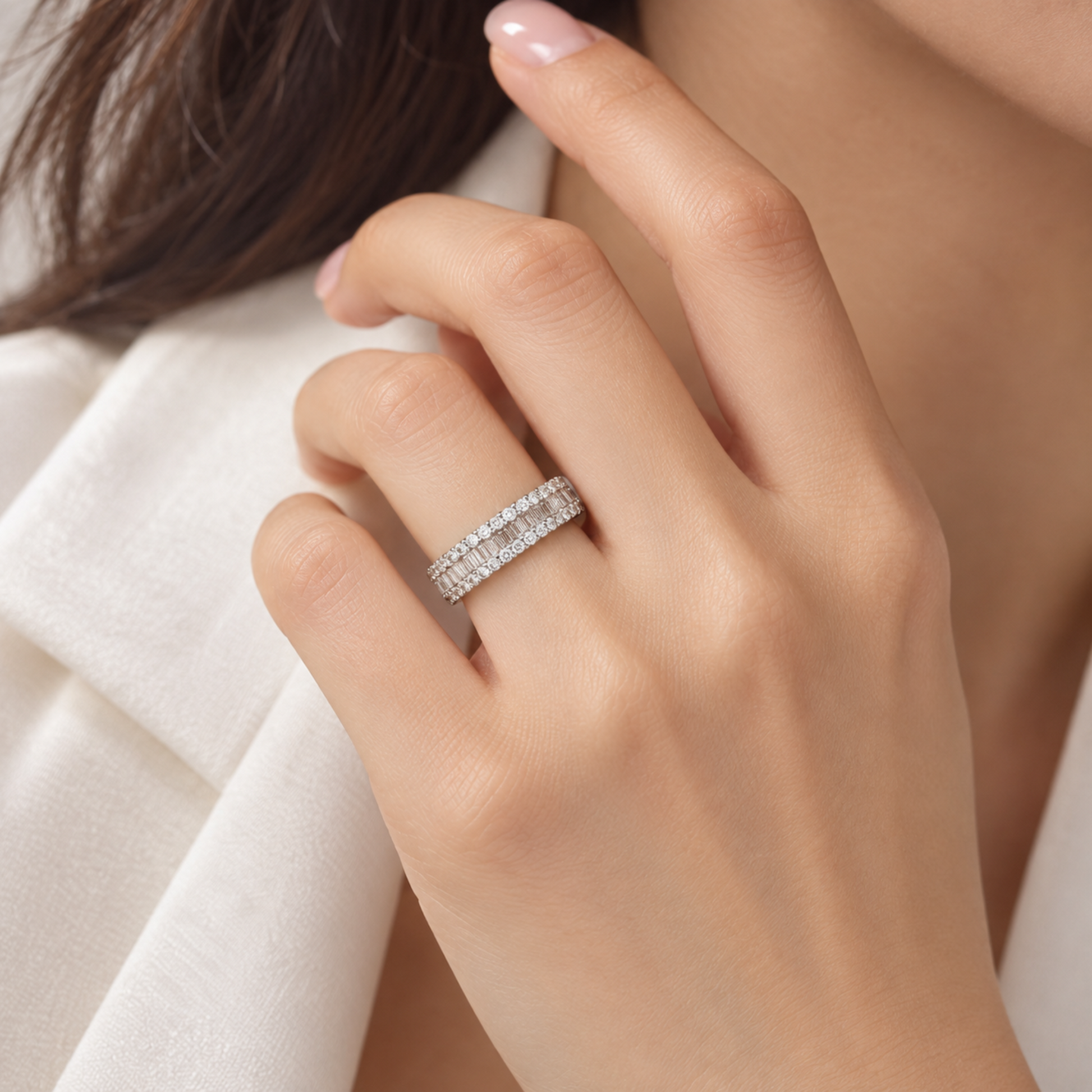 A close-up of a woman's hand wearing a silver band ring set with small clear diamonds, styled with a white blazer.