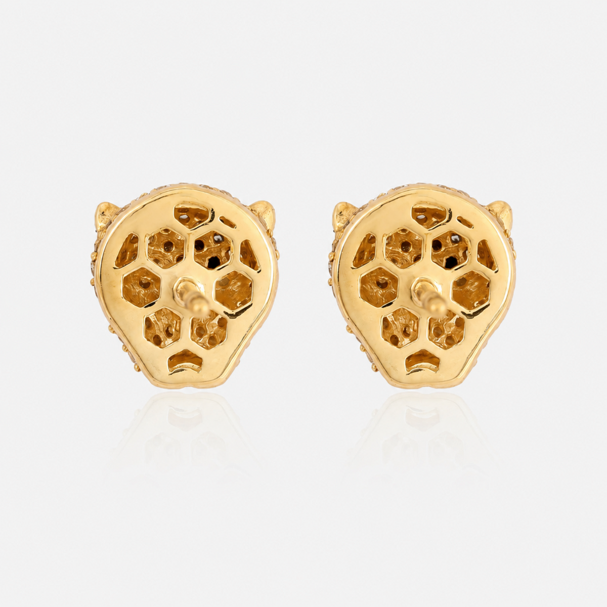 A pair of gold stud earrings shaped like stylized animal heads with openwork geometric patterns, displayed on a light gray reflective surface.