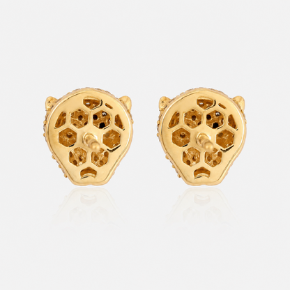 A pair of gold stud earrings shaped like stylized animal heads with openwork geometric patterns, displayed on a light gray reflective surface.