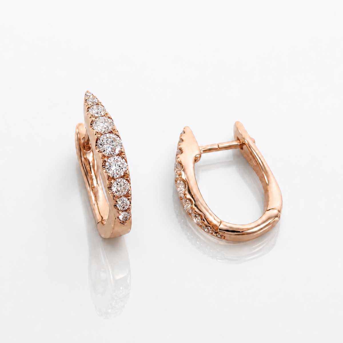 A pair of rose gold huggie hoop earrings with pavé-set round diamonds, displayed on a clean white reflective surface.