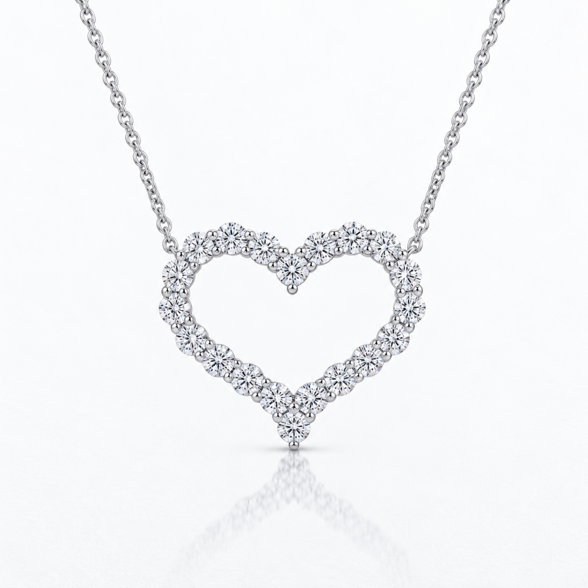 A silver-toned open heart pendant necklace paved with small clear diamonds, suspended from a delicate chain on a clean white background with a soft reflection below.