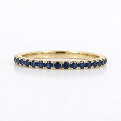 A yellow gold eternity ring set with round blue sapphires, shown on a clean white background with a soft reflection.
