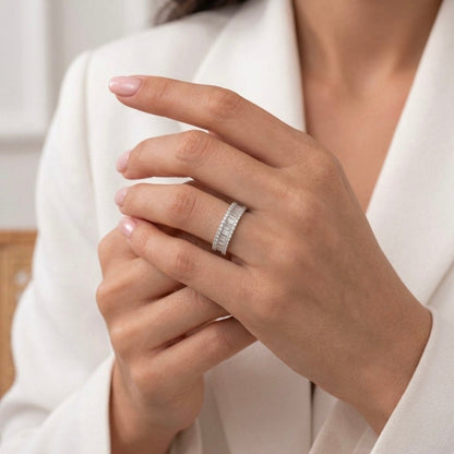 A close-up of a woman's hands wearing a slim silver band ring with a row of small diamonds, styled with a white blazer.