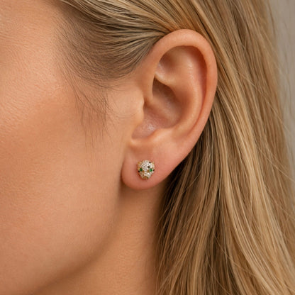 A close-up of a woman's ear wearing a small round stud earring with a gold-toned halo setting and clear stones.