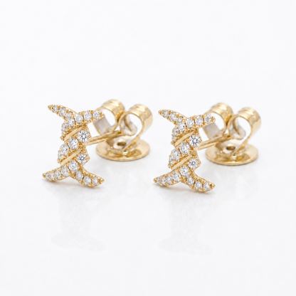 A pair of gold stud earrings with a twisted, star-like design paved with small clear diamonds, shown on a clean white background.
