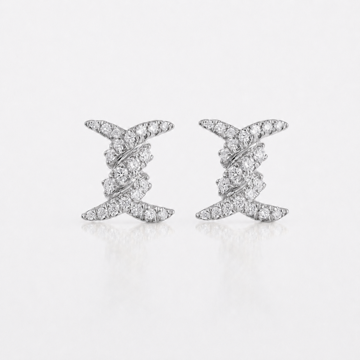 A pair of silver-toned stud earrings with a twisted, layered design set with small clear diamonds, displayed on a clean white background with a soft reflection.