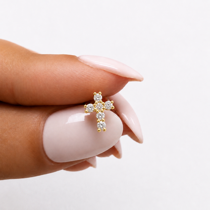 Single yellow gold natural diamond cross stud earring held between fingers showing scale