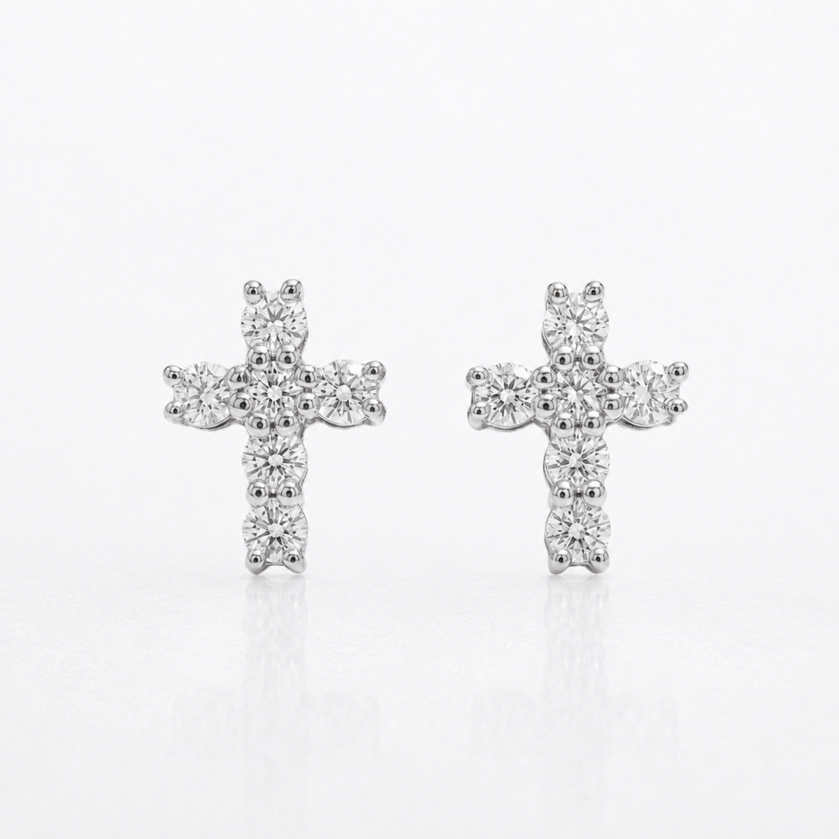 Pair of white gold natural diamond cross stud earrings on reflective surface