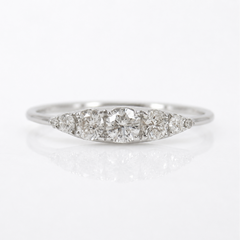A silver-colored diamond ring with a marquise-shaped cluster setting featuring a central round diamond and three smaller diamonds on either side, set against a clean white background with a soft reflection.
