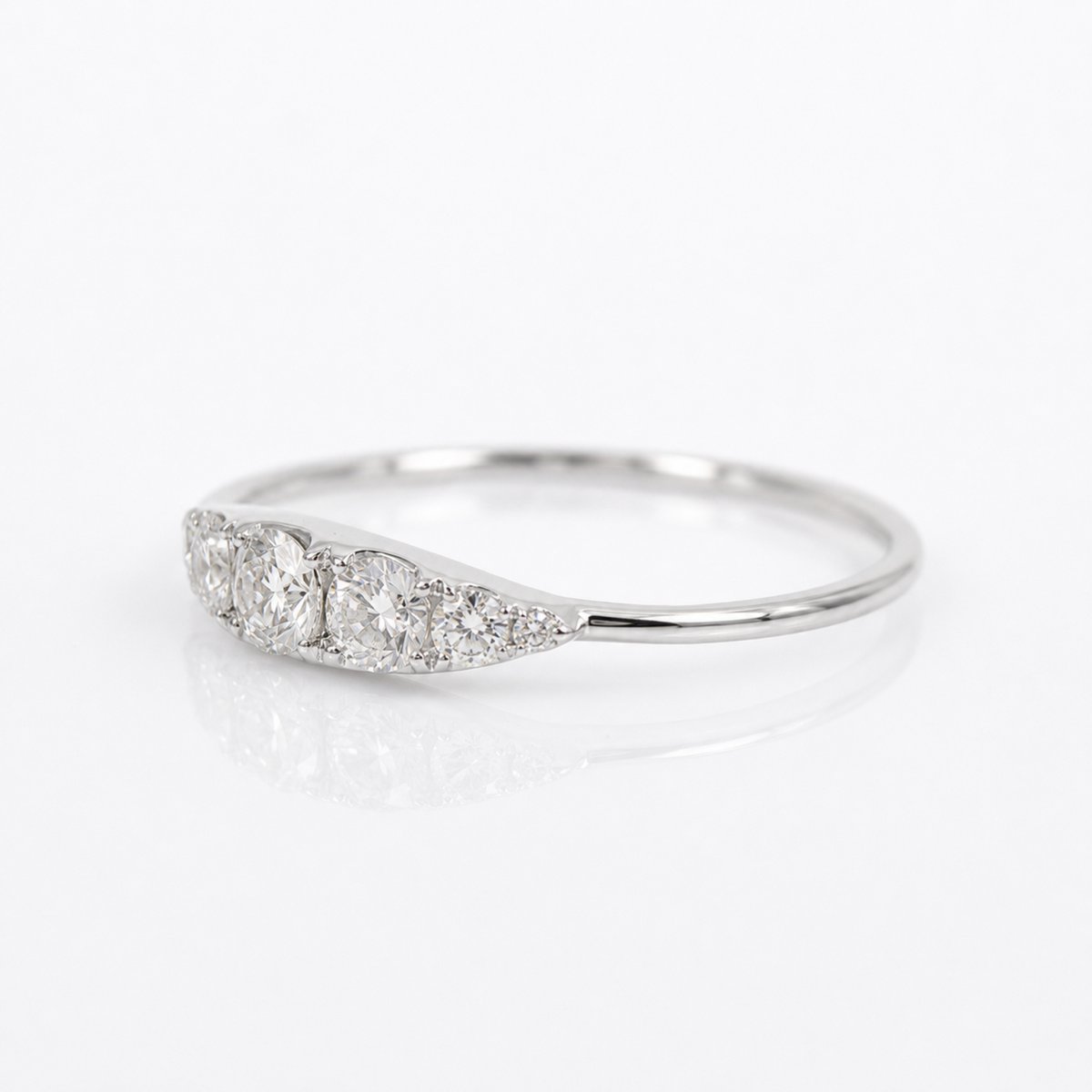A silver three-stone diamond ring with a curved, tapered setting, photographed on a clean white reflective surface.
