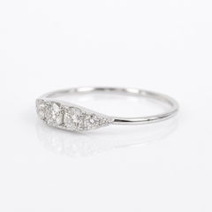 A silver three-stone diamond ring with a curved, tapered setting, photographed on a clean white reflective surface.
